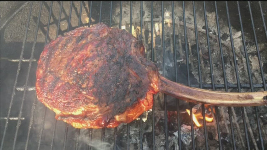 tomahawk steak sizzling on an open grill